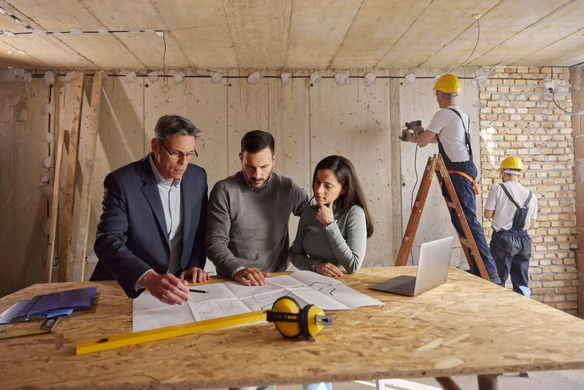 People reviewing construction plans in unfinished room.